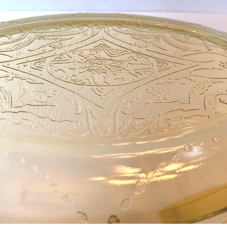 May include: A vintage, clear glass plate with an embossed, intricate design. The design features a repeating pattern of stylized flowers and leaves.