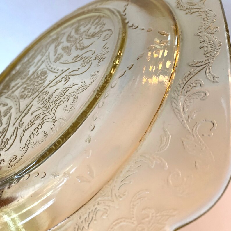 May include: A vintage yellow glass plate with a floral design. The plate has a scalloped edge and a raised rim.