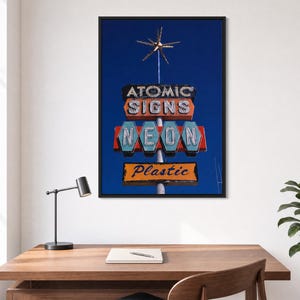May include: A framed wall art print featuring a vintage-style sign against a deep blue sky. The sign displays the text ATOMIC SIGNS, NEON, and Plastic in stacked rectangular and hexagonal panels, topped with a metallic starburst ornament.