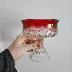 以下が含まれることがあります： 赤いガラスのトップを持つ透明なガラスの台座。台座は、小さな隆起したドットでテクスチャ加工されたデザインです。