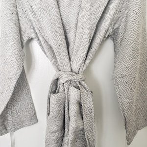 May include: A gray and white patterned robe with a hood and a tie belt. The robe has two pockets on the front.