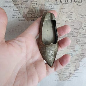 Può includere: Un posacenere in ottone a forma di scarpa con intricati disegni floreali.