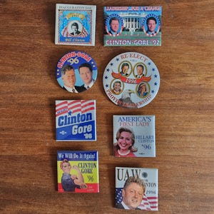 May include: A collection of eight political campaign badges featuring images of Bill Clinton, Al Gore, and Hillary Clinton. The badges are from the 1992 and 1996 presidential elections. The badges feature slogans such as "Leadership for a Change", "Re-Elect", "America's First Lady", and "We Will Do It Again!"