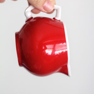 Może przedstawiać: Cukiernica w kolorze czerwonym z białym uchwytem i obrzeżem. Cukiernica wykonana jest z ceramiki i ma błyszczące wykończenie.