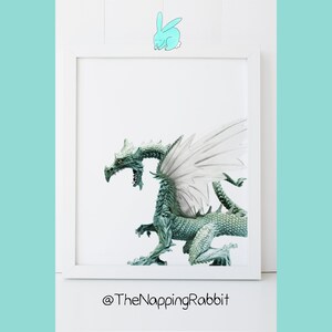 May include: A white framed picture with a green dragon with white wings on a white background. The text "@TheNappingRabbit" is below the picture.