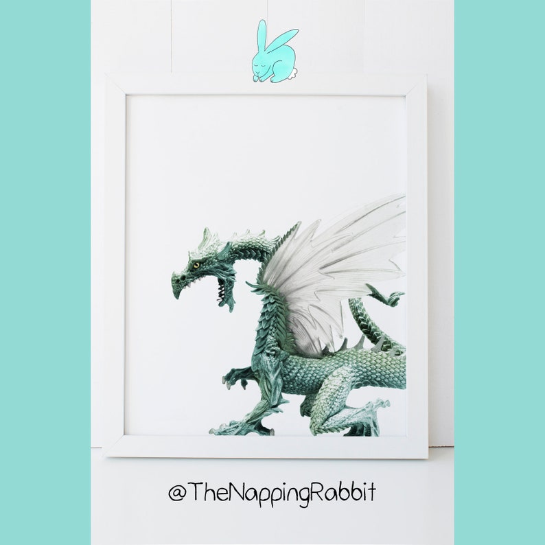 May include: A white framed picture with a green dragon with white wings on a white background. The text "@TheNappingRabbit" is below the picture.