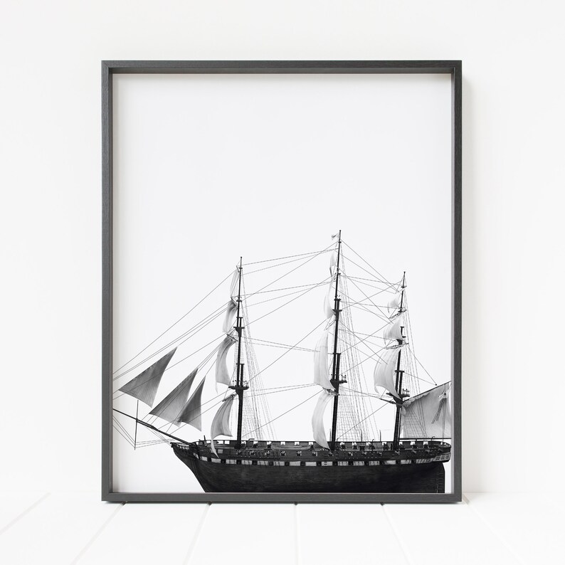 May include: A black and white photograph of a tall ship with sails billowing in the wind. The ship is framed in a black frame.