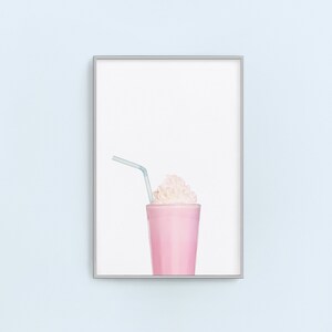 May include: A framed print of a pink milkshake with whipped cream and a blue straw. The background is white.