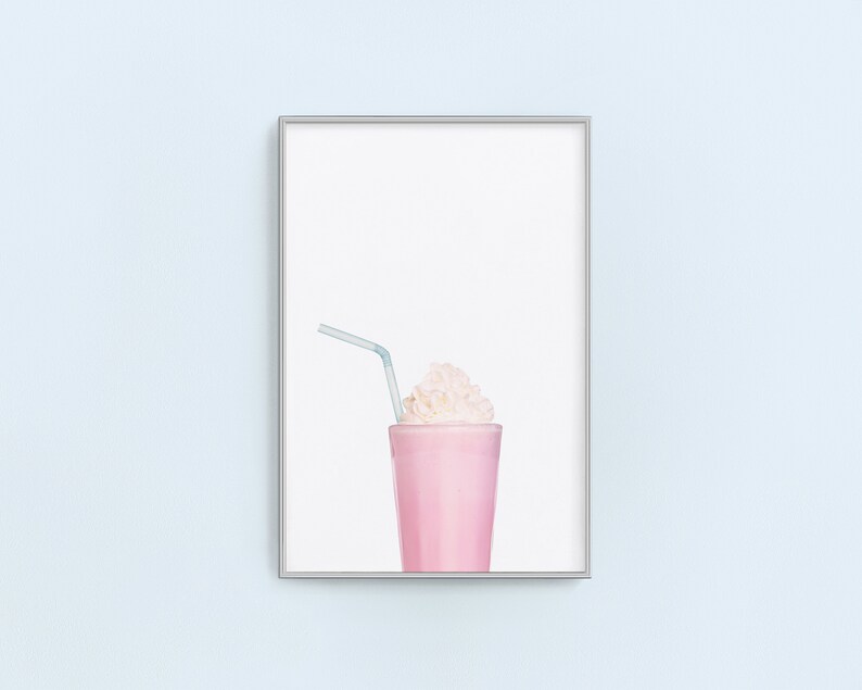 May include: A framed print of a pink milkshake with whipped cream and a blue straw. The background is white.