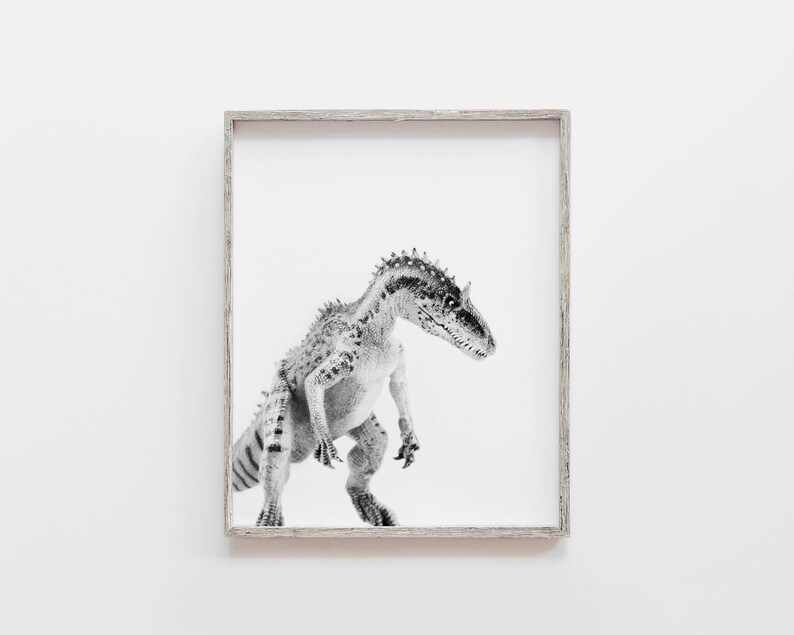 May include: Black and white photograph of a dinosaur in a simple wooden frame. The dinosaur is standing on a white background.