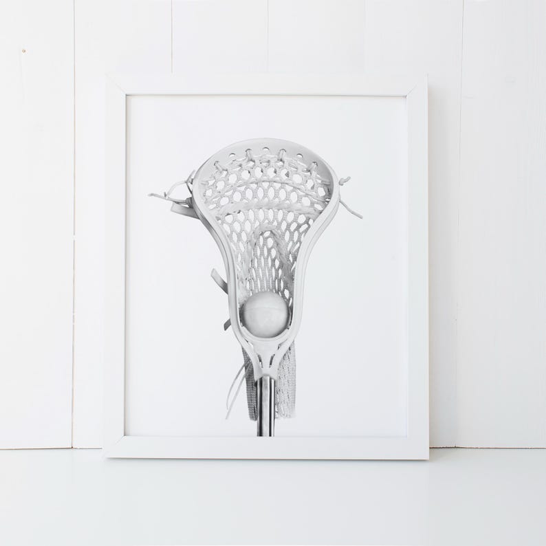 K&ouml;nnte beinhalten: Ein wei&szlig;er Lacrosse-Schl&auml;ger mit einem wei&szlig;en Ball im Netz. Der Schl&auml;ger ist scharf gestellt und der Hintergrund ist verschwommen.
