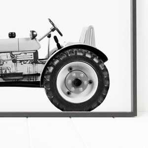 May include: Black and white photograph of a vintage tractor with a single large tire in focus.