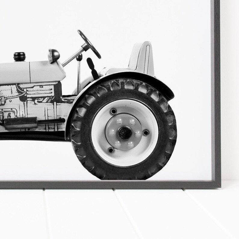May include: Black and white photograph of a vintage tractor with a single large tire in focus.