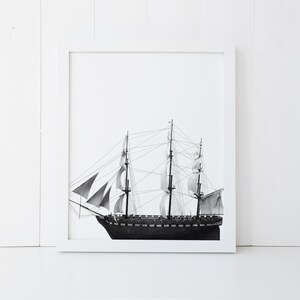 May include: A black and white photograph of a ship with sails, framed in a white frame.