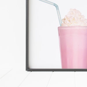 May include: A pink milkshake with whipped cream and a blue straw in a glass. The milkshake is in a black frame.