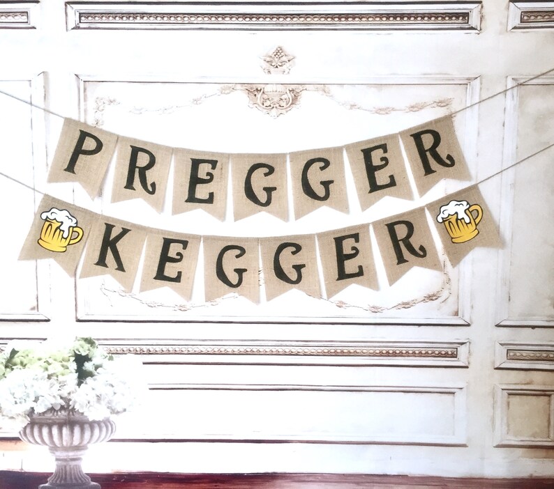 May include: A burlap banner with the text "Pregger Kegger" in black letters. The banner has two yellow beer mugs with white foam on top.