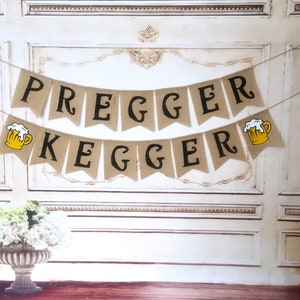 May include: A burlap banner with the text "Pregger Kegger" in black letters. The banner is decorated with two yellow beer mugs with white foam.