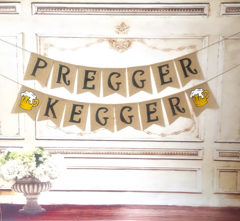 May include: A burlap banner with the text "Pregger Kegger" in black letters. The banner is decorated with two yellow beer mugs with white foam.