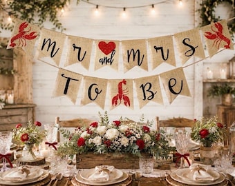 May include: A two-tiered burlap banner featuring red lobster illustrations, a red heart, and black cursive text that reads "mr and mrs to be". The banner is constructed from tan fabric pennants strung together on a thin, light-colored cord.