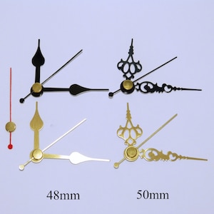 K&ouml;nnte beinhalten: Vier Uhrzeiger, zwei schwarz, zwei goldfarben, mit goldenen Akzenten. Die Zeiger sind 48 mm und 50 mm lang.