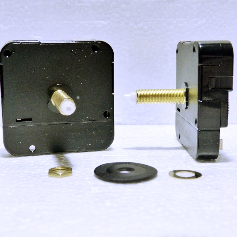 K&ouml;nnte beinhalten: Zwei schwarze Uhrwerke mit goldfarbenen Wellen und wei&szlig;en Kunststoffspitzen. Die Uhrwerke befinden sich auf einer wei&szlig;en Oberfl&auml;che mit einer schwarzen Unterlegscheibe, einer goldfarbenen Mutter und einer silbernen Unterlegscheibe.