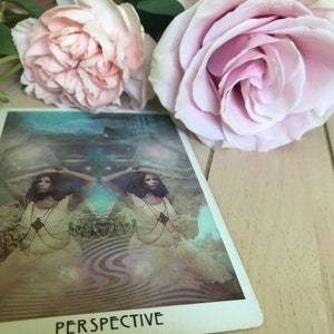 Könnte beinhalten: Eine Tarotkarte mit dem Wort "Perspektive" darauf gedruckt. Die Karte zeigt eine Frau mit erhobenen Armen, die vor einem wirbelnden, abstrakten Hintergrund steht.