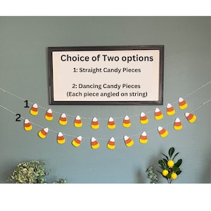 May include: Two strands of candy corn garland, each with 10 candy corn pieces. The candy corn is yellow, orange, and white. A framed sign above the garland reads "Choice of Two options" and lists the garland options.