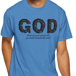 May include: A light blue t-shirt with the word "GOD" in a floral design. Below the word "GOD" is the text "What are you trying to fill your GOD shaped hole with?"