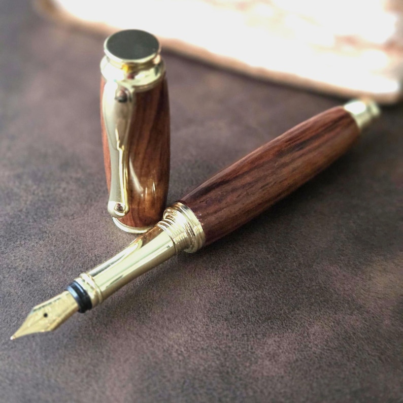 Handcrafted reddish-brown wooden fountain pen with gold nib and cap displayed on soft brown fabric background.