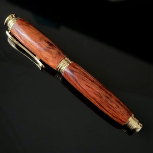 Handcrafted wooden fountain pen cap showing smooth reddish wood grain and gold clip on reflective black surface.