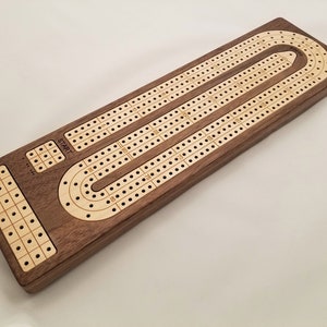 May include: A wooden cribbage board with a dark brown frame and a light wood playing surface. The board has three tracks with numbered holes for pegging, and a start and finish area. The word "START" is visible.