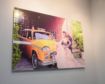 Op de afbeelding: Een stel poseert voor een gele taxi. De vrouw draagt een roze trouwjurk en de man draagt een zwart pak. De taxi heeft een "TAXI"-bord op het dak.