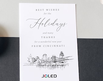 May include: A white holiday greeting card with the text "Best Wishes for the Holidays" in elegant script. Below is a detailed black and white illustration of a city skyline, with the text "From Cincinnati" and the brand name "JOLED".
