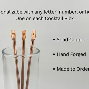 May include: Three copper cocktail picks in a glass. The picks are hand-forged and personalized with a heart, the letter "B", and the number "7".  Solid copper, hand forged, made to order.