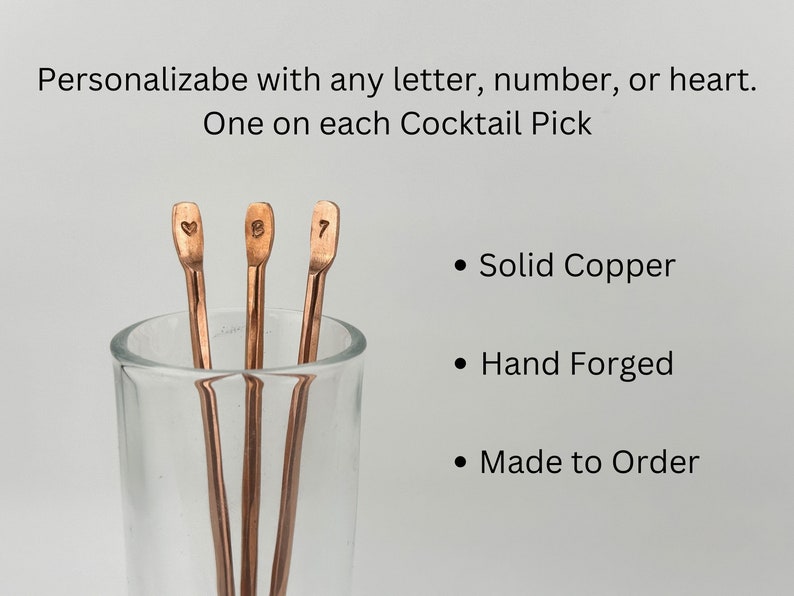 May include: Three copper cocktail picks in a glass. The picks are hand-forged and personalized with a heart, the letter "B", and the number "7".  Solid copper, hand forged, made to order.