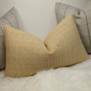 May include: A close-up of three decorative throw pillows. The central pillow is a golden yellow with a diamond pattern. Two other pillows are visible, one on each side, in a gray plaid pattern. The pillows are resting on a white, fluffy surface.