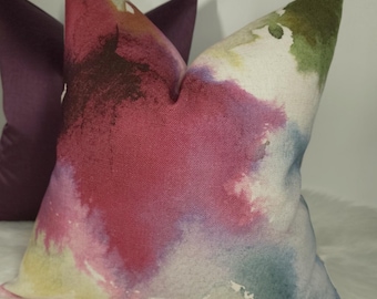 May include: A decorative throw pillow with a watercolor-style design featuring shades of pink, purple, green, and blue.
