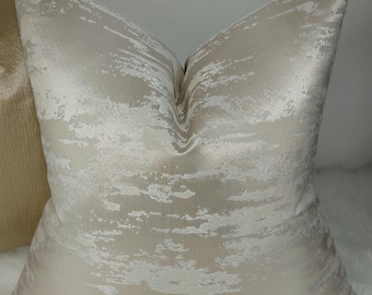 May include: A soft, cream-colored throw pillow with a subtle, abstract pattern in a lighter shade of cream. The pillow has a smooth, silky texture.