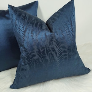 Puede incluir: Dos almohadas de sofá azules con un patrón de helecho. Las almohadas están hechas de una tela suave y texturizada.