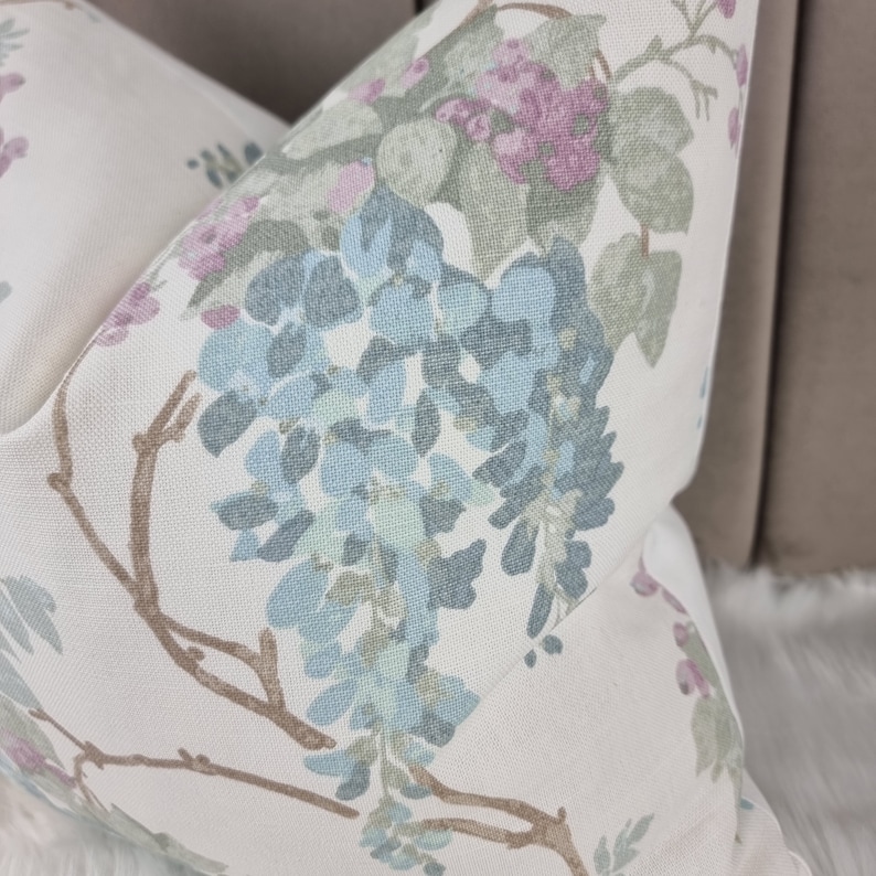 May include: A white pillow with a floral pattern featuring blue, green, and pink flowers. The pillow has a white background and the flowers are scattered across the fabric.