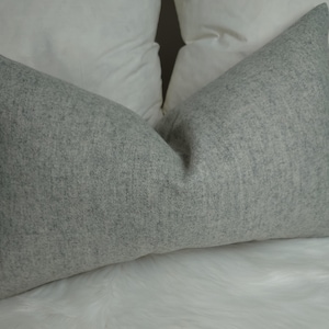 Peut inclure: Un oreiller rectangulaire gris avec un tissu doux et texturé. L'oreiller est posé sur une surface blanche.