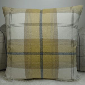 Può includere: Cuscino quadrato decorativo con motivo a quadri giallo, crema e grigio. Il design presenta linee che si intersecano formando una griglia. Il tessuto ha un aspetto strutturato. Per divano o letto.