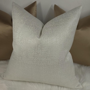 May include: A white pillow with a textured surface. The pillow is surrounded by two brown pillows.