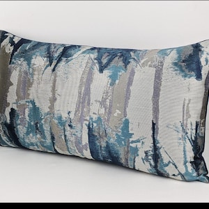 Puede incluir: Una almohada rectangular de color azul, gris y blanco con un patrón y un borde azul oscuro.