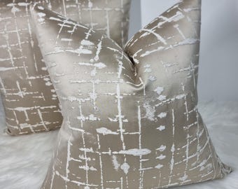 May include: Two decorative throw pillows with a geometric pattern in shades of beige and white. The pillows are made of a soft, textured fabric.