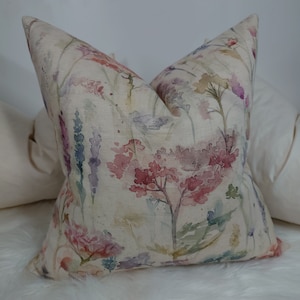 May include: A cream-colored pillow with a watercolor floral pattern in shades of pink, purple, and green. The flowers are abstract and have a soft, faded look.