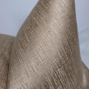 May include: A close-up of a gold-coloured fabric with a textured, woven pattern. The fabric has a subtle sheen and a slightly raised surface.