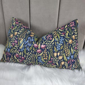 Op de afbeelding: Een donkerblauw kussen met een bloemenpatroon met roze, gele en groene bloemen. Het kussen is gemaakt van een zachte, textuurrijke stof.