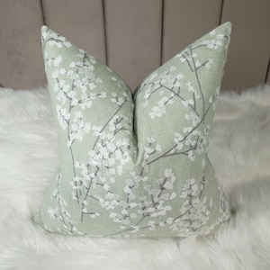 Può includere: Un cuscino verde con un ricamo floreale bianco. Il cuscino è realizzato in un tessuto morbido e testurizzato.