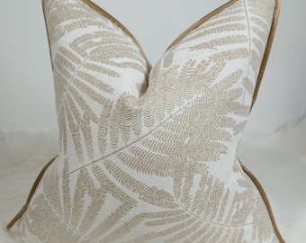 May include: A white throw pillow with a gold fern pattern and a gold trim. The pillow is made of a soft, textured fabric.